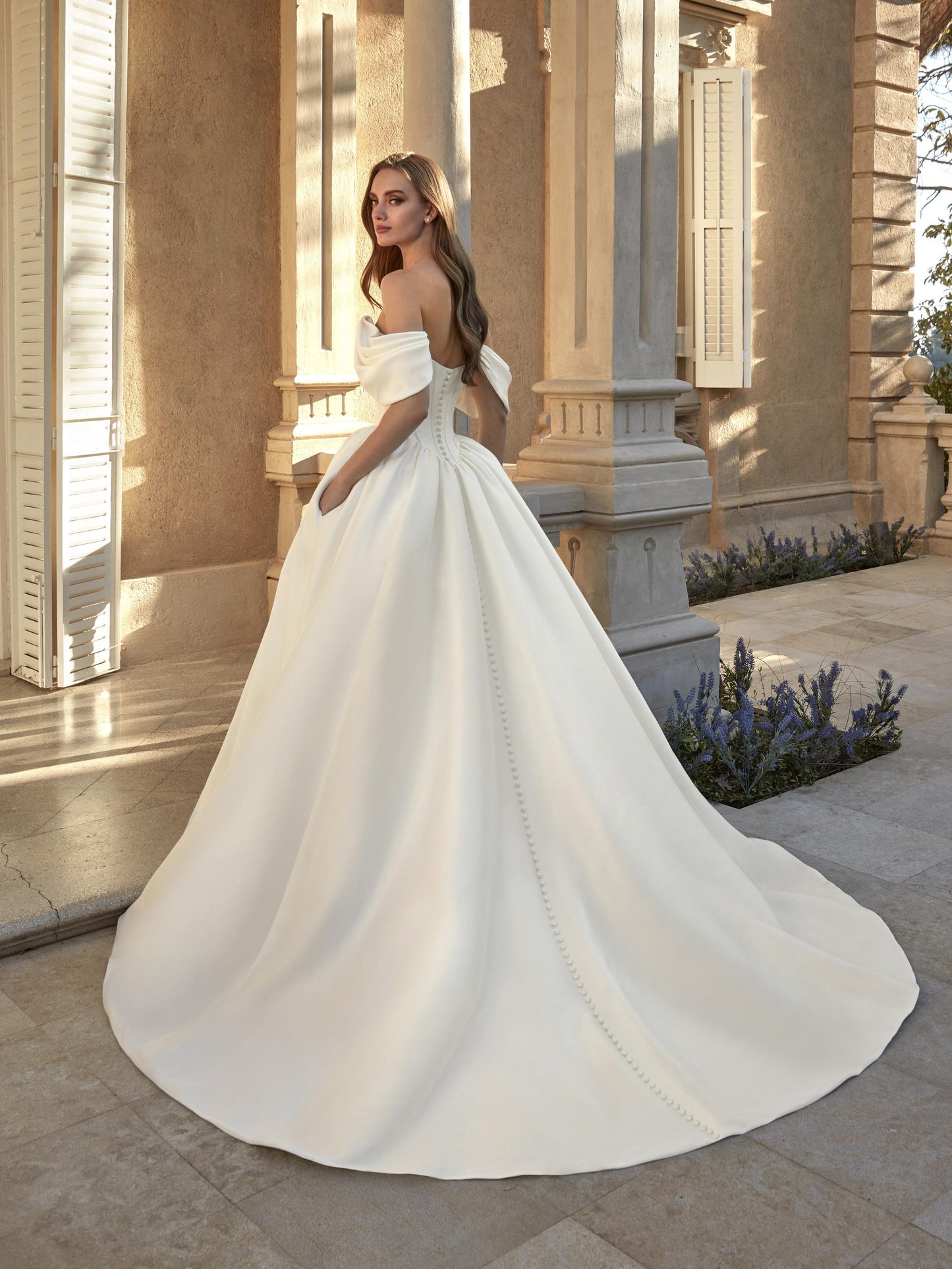 Back view of the Anabela Mikado ball gown wedding dress featuring off-the-shoulder straps and a cathedral train accented with buttons.