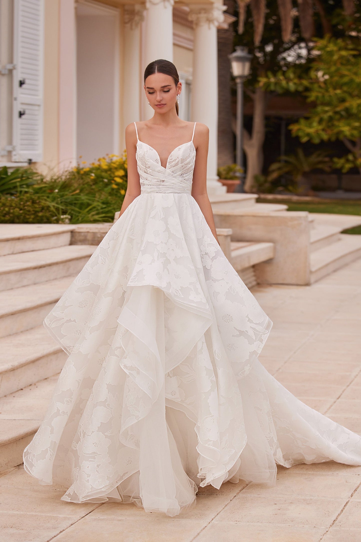 Front view of the Arran wedding dress featuring a plunging neckline, thin spaghetti straps, a draped floral jacquard bodice, and a tiered A-line skirt.