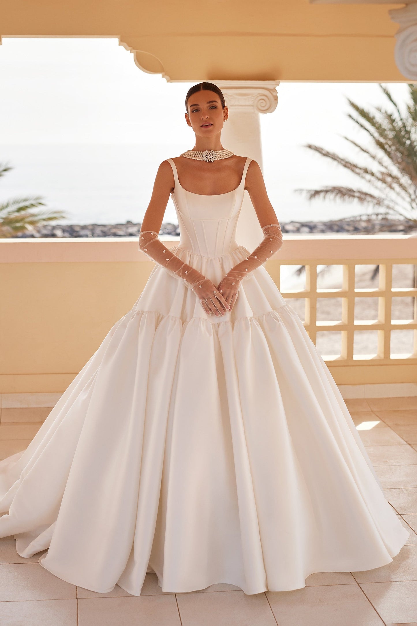 Front view of the Britania ball gown wedding dress featuring a structured square neckline, exposed boning, and a voluminous, tiered Mikado skirt with a dramatic basque waist.