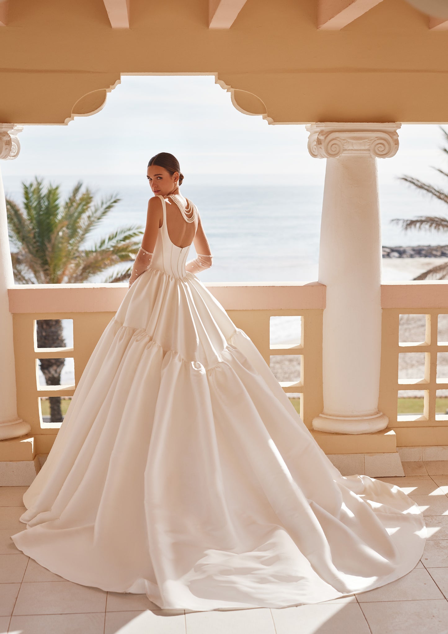 Back view of the Britania ball gown wedding dress showcasing a low scoop back, exposed boning, and a dramatic tiered Mikado skirt with a cathedral train.