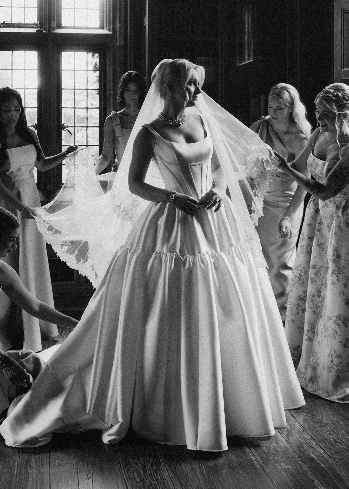 Krismil Bride Weronika surrounded by bridesmaids wearing a regal Mikado ball gown with a veil in a bridal suite.