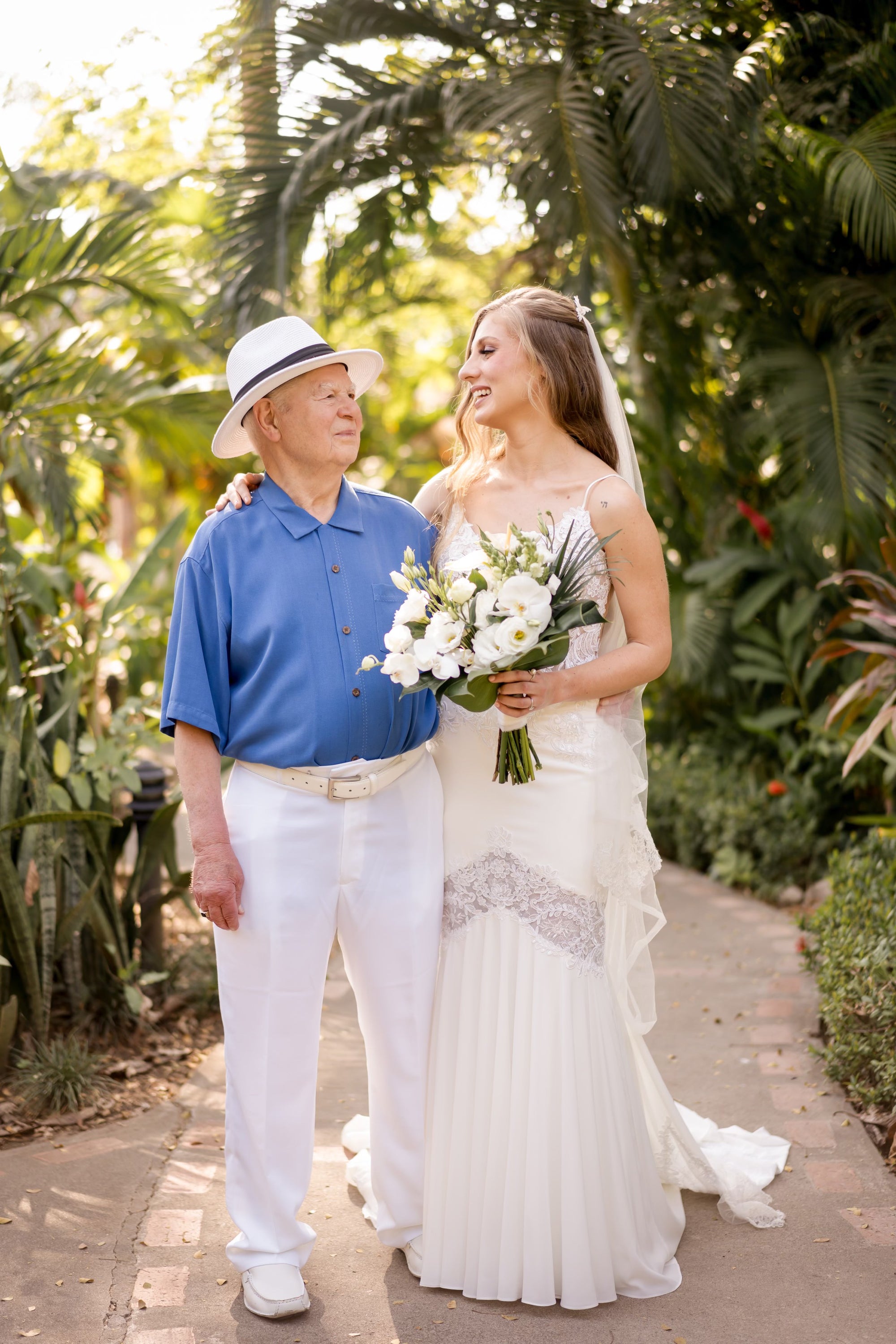Bride Alina in a lace mermaid wedding dress by Krismil Bridal, holding a bouquet and smiling at her grandfather during her wedding in Costa Rica.