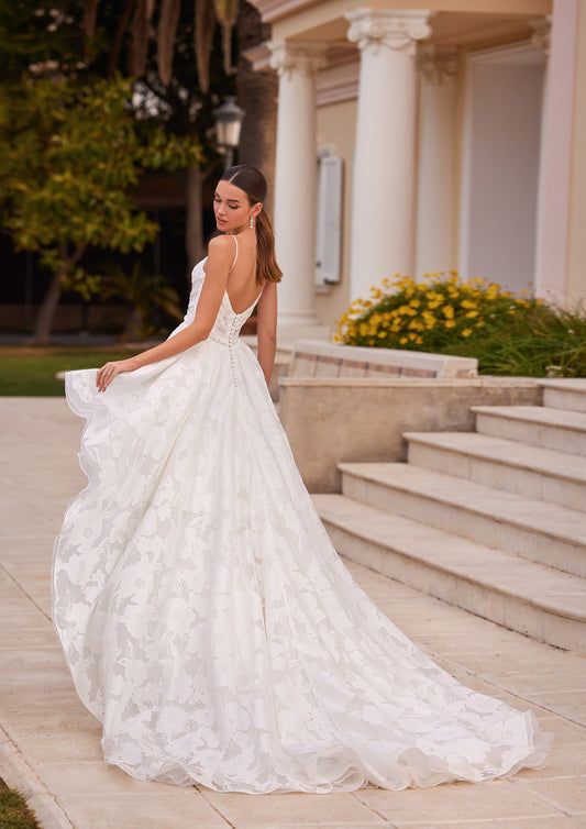 Back view of the Arran A-Line wedding dress featuring a low open back, thin spaghetti straps, and a flowing jacquard skirt with buttons down the back.