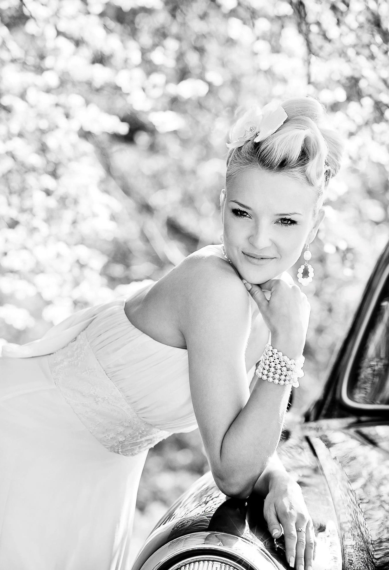 Bride leaning on a vintage car in a sleeveless chiffon wedding dress by Krismil Bridal, smiling during her wedding in Lithuania.
