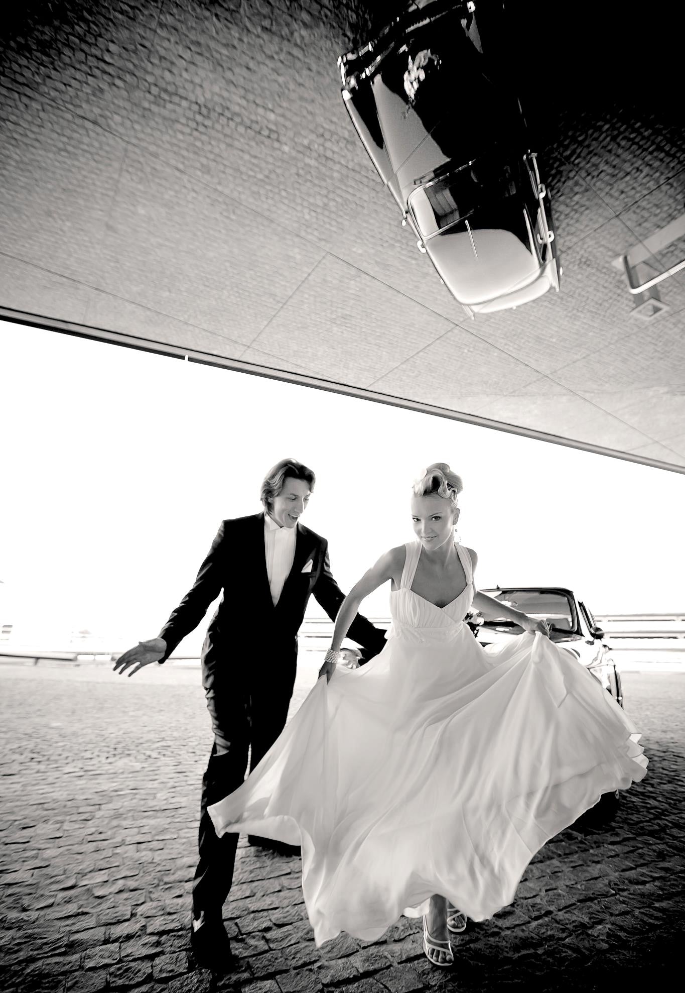 Bride in a flowing chiffon A-line wedding dress by Krismil Bridal and groom joyfully running together during their wedding in Lithuania.
