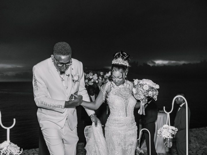 Bride Brittany in a beaded mermaid wedding dress by Krismil Bridal, walking with her husband Kenard during their wedding at Ocean Cliff Hotel in Negril, Jamaica.