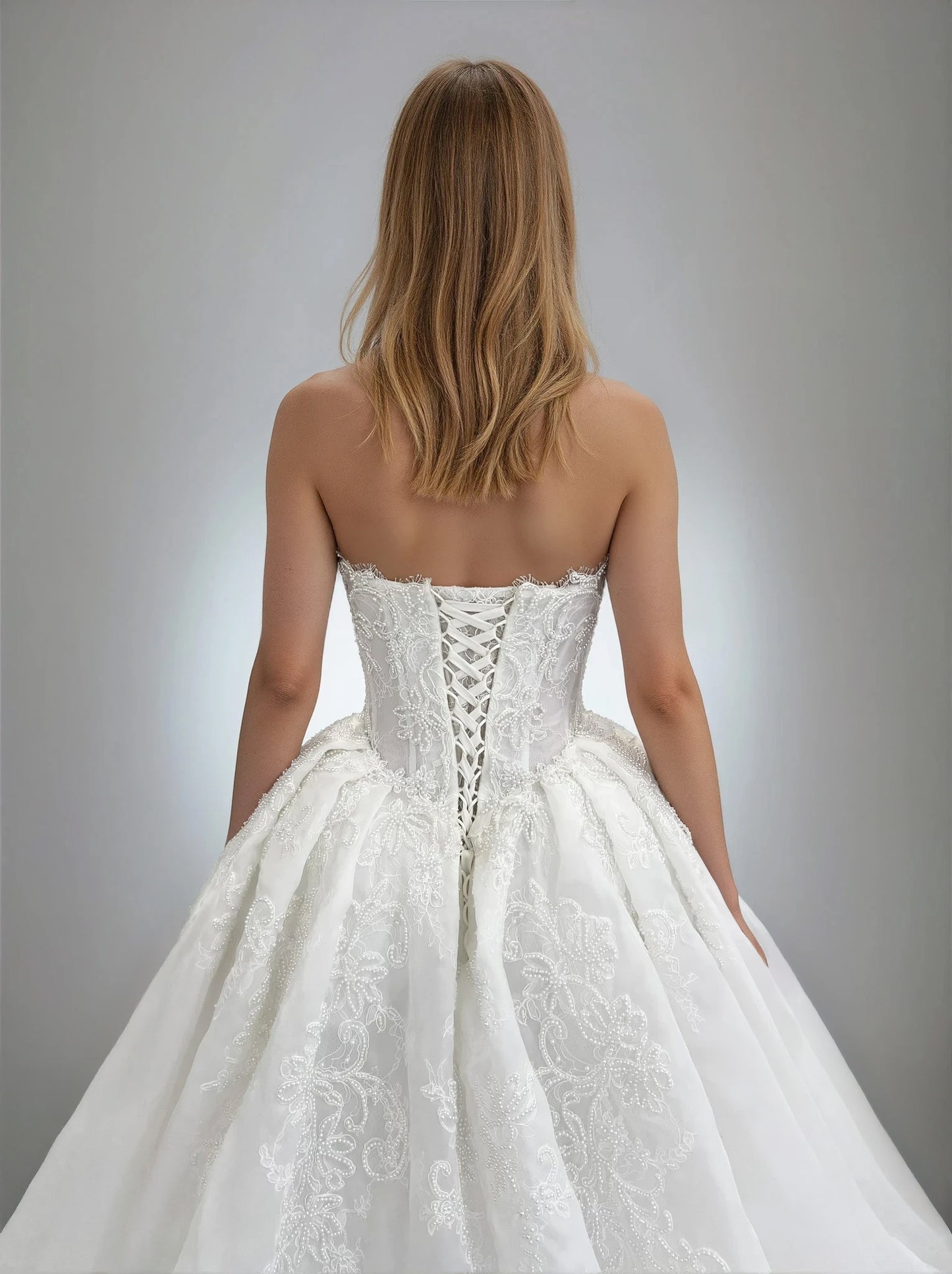 Close-up back view of the Claudia ball gown wedding dress showcasing a strapless lace-up corset bodice with intricate pearl-embellished embroidery and a voluminous pleated skirt.