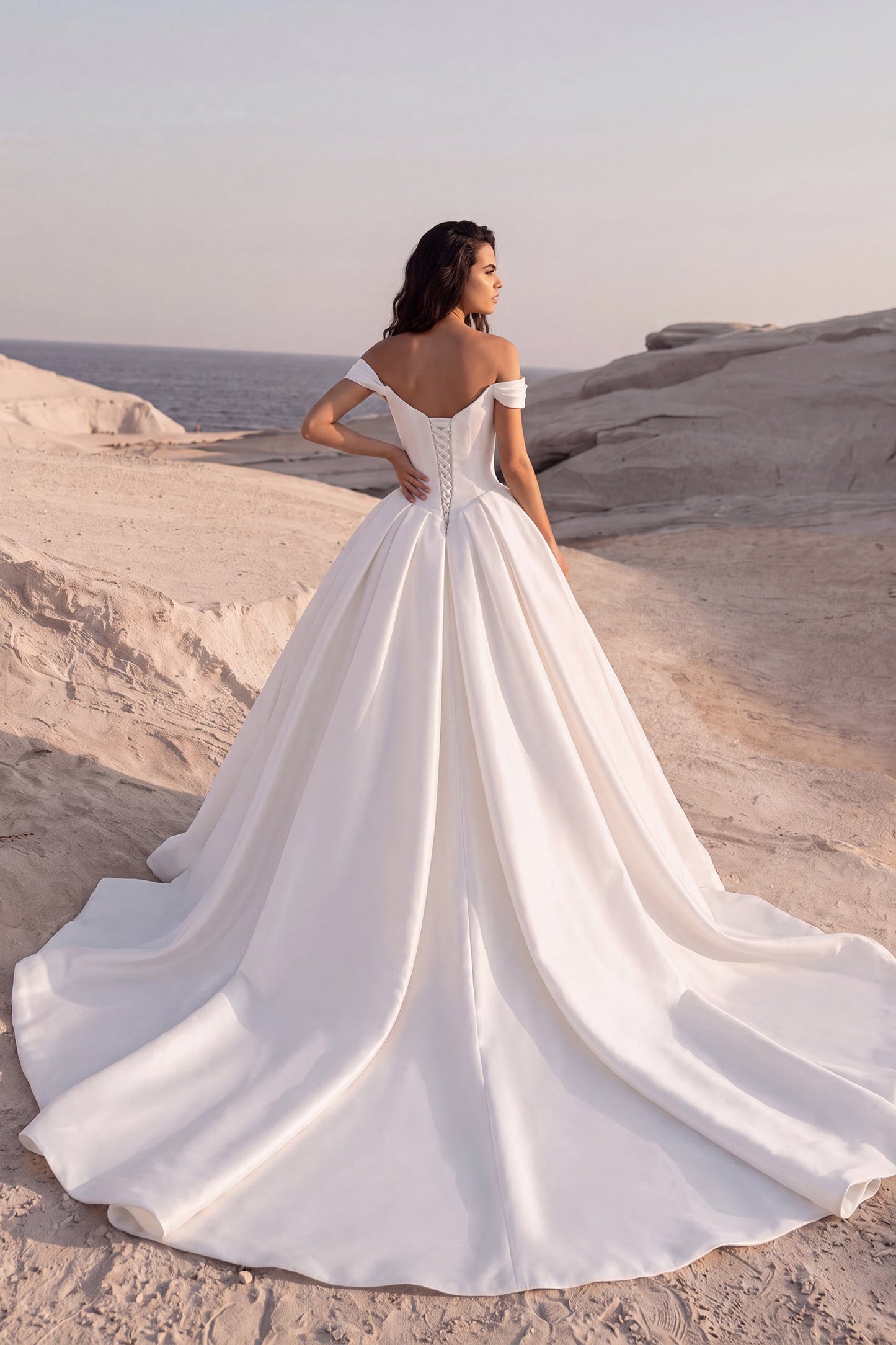 Back view of the Eliana wedding dress featuring an off-the-shoulder neckline, lace-up corset back, and a voluminous Mikado ball gown with a cathedral train.