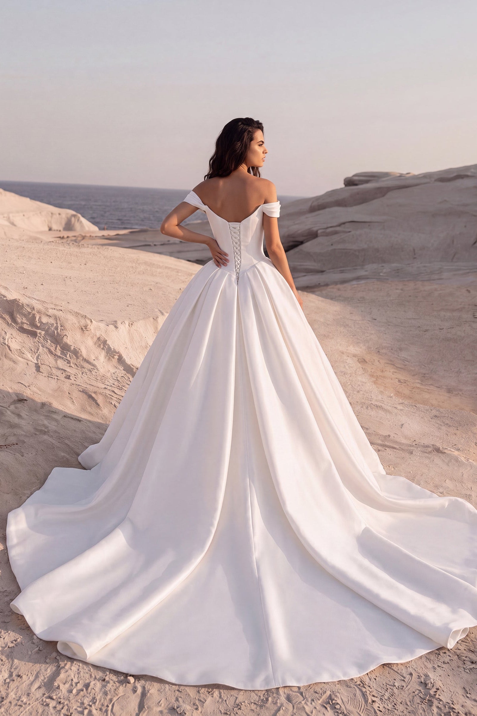 Back view of the Eliana wedding dress featuring an off-the-shoulder neckline, lace-up corset back, and a voluminous Mikado ball gown with a cathedral train.