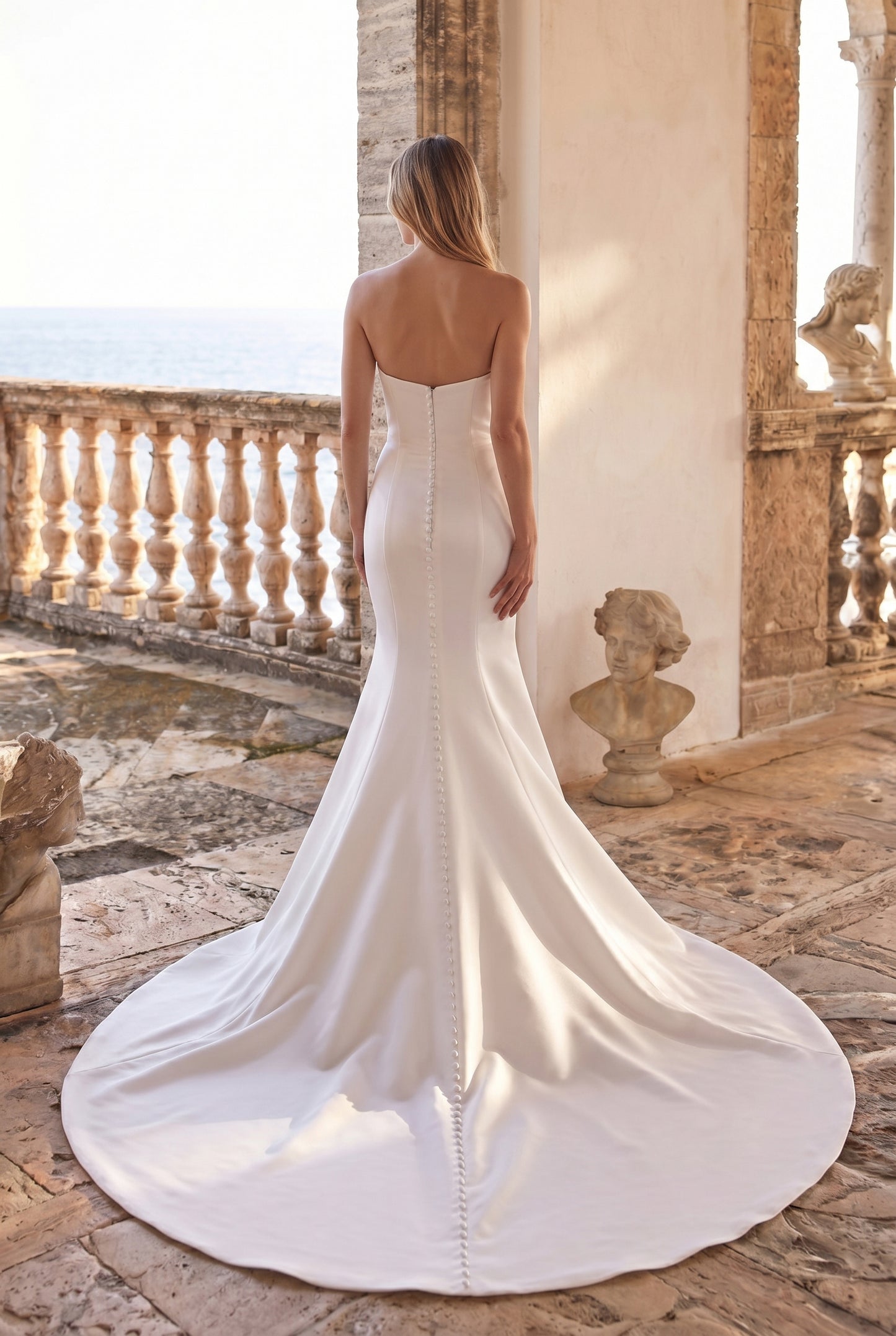 Back view of the Harper wedding dress featuring a strapless neckline, smooth satin fit-and-flare silhouette, and a row of buttons down the back flowing into a cathedral train.
