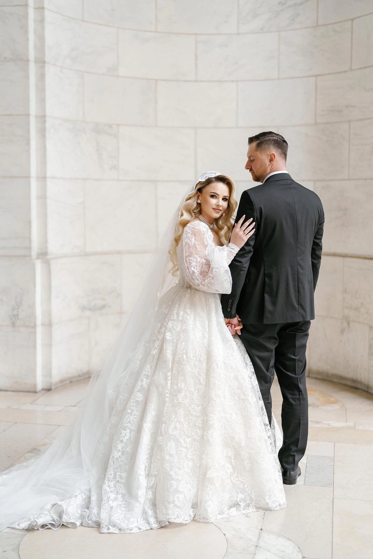Bride Khristina in a stunning lace ball gown and groom Andriy holding hands in an elegant marble venue, showcasing timeless love and sophistication.