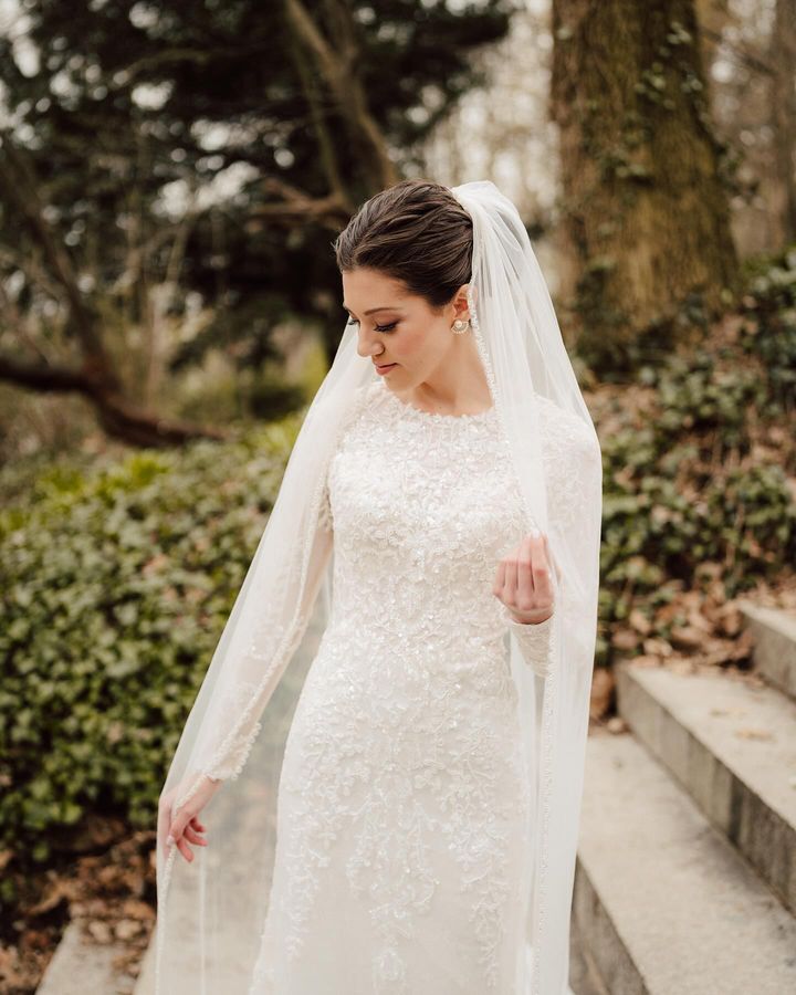 Bride Malka in a modest lace mermaid wedding dress by Krismil Bridal, elegantly posed in a natural setting.