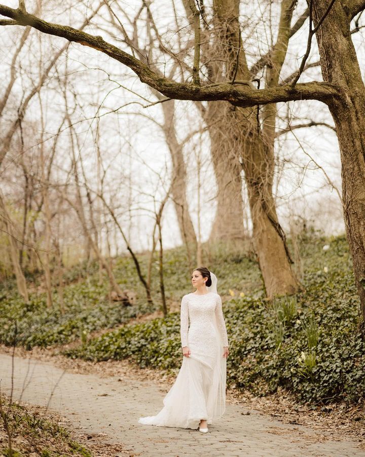 Bride Malka in a modest lace mermaid wedding dress by Krismil Bridal, walking through a wooded path.