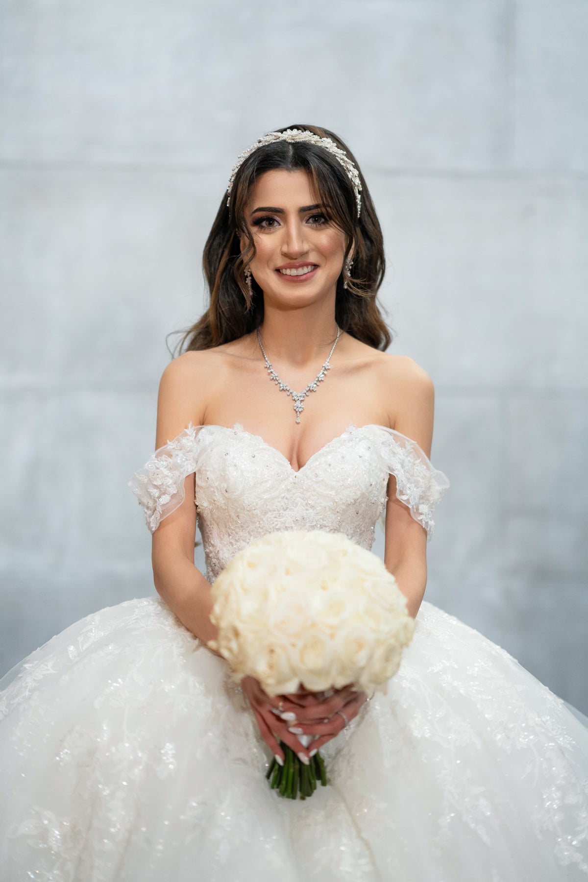 Bride Margaret in an off-the-shoulder ball gown with a sweetheart neckline by Krismil Bridal, holding a white rose bouquet in New York City.