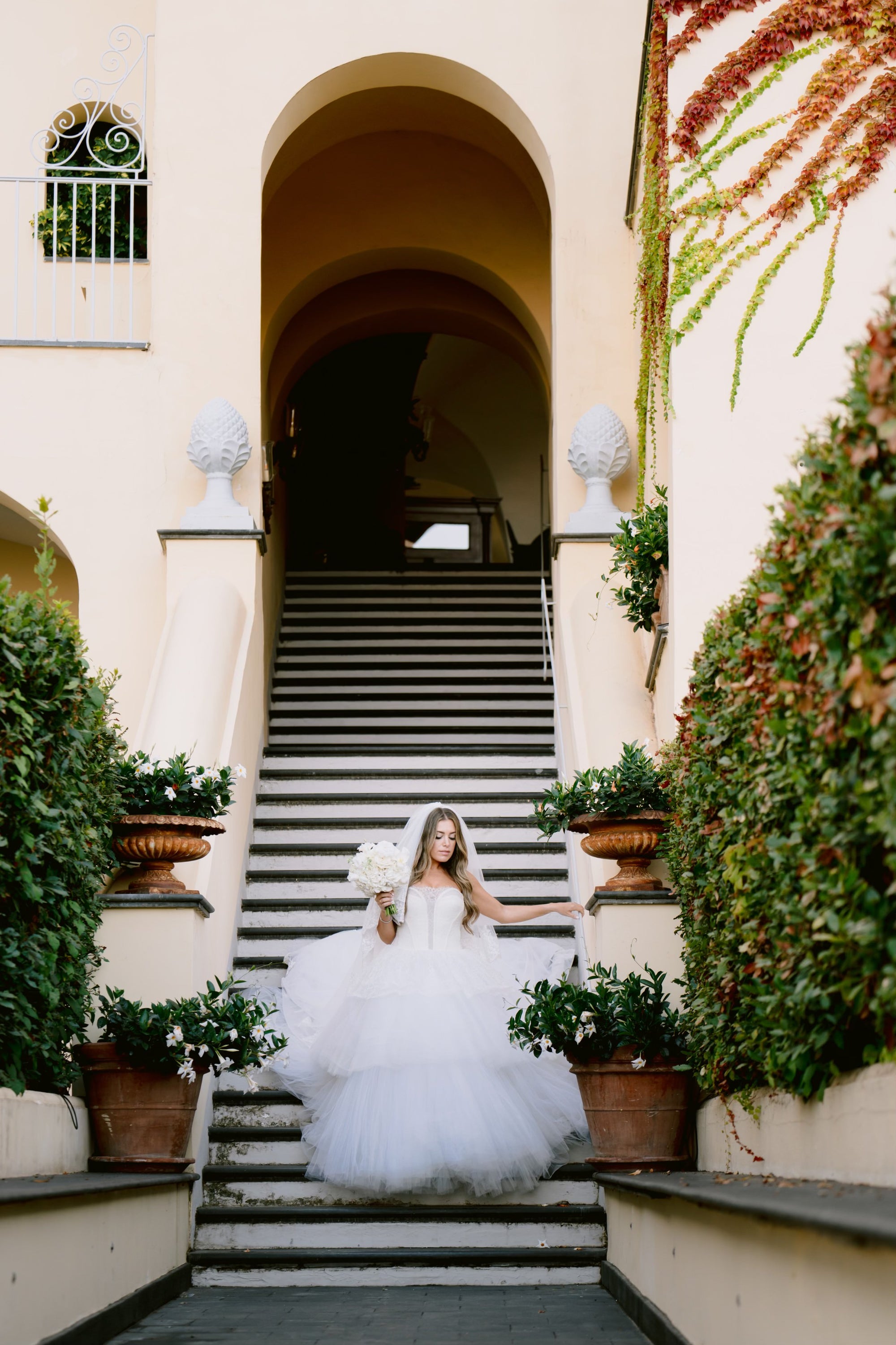 Bride Michelle in a tulle wedding dress by Krismil Bridal, holding a bouquet and descending stairs at her wedding in Ravello, Italy.