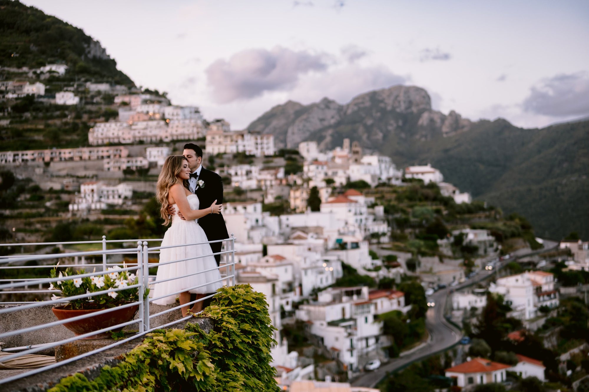 Bride Michelle and her husband embracing at their wedding in Italy, overlooking the scenic town and mountains.