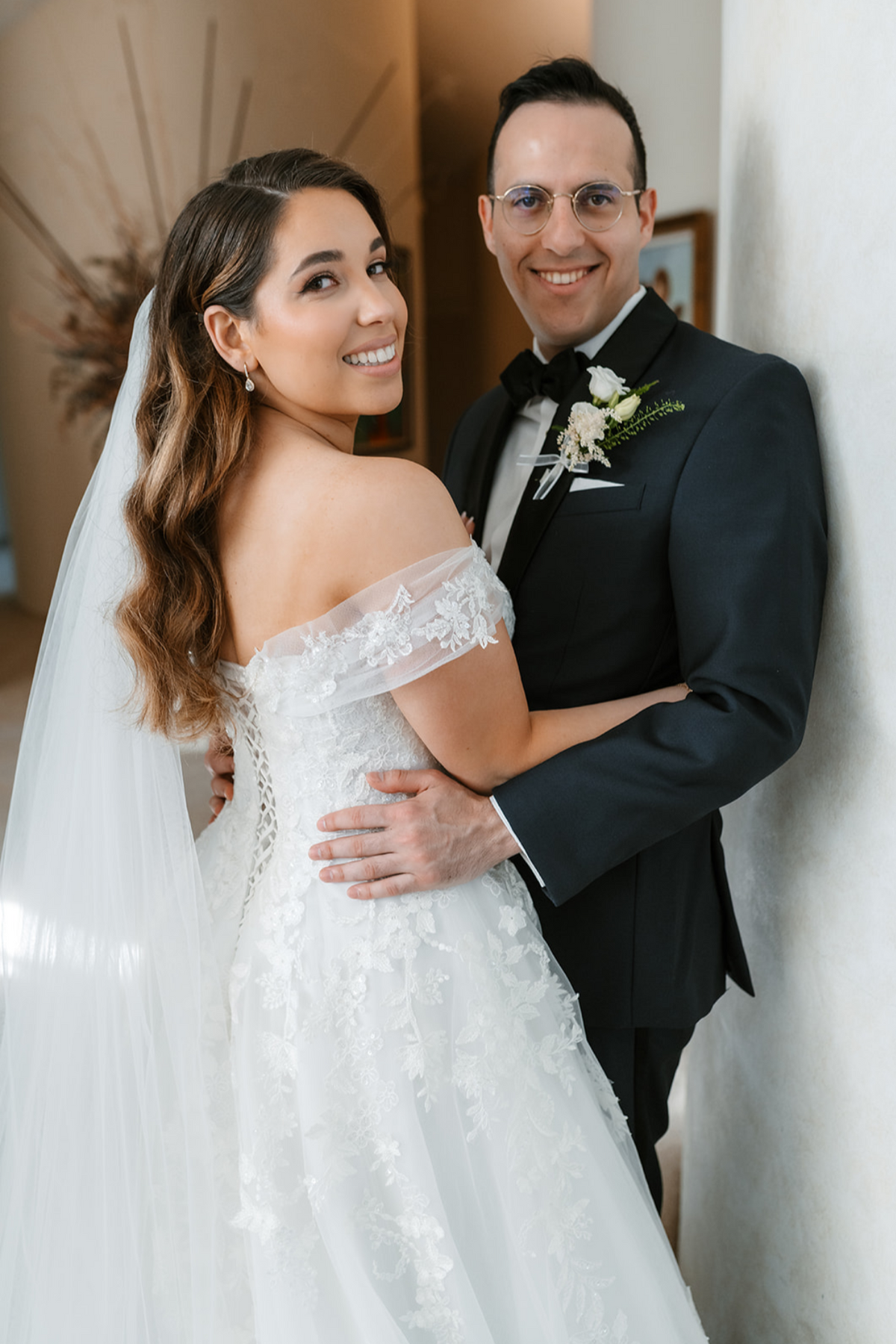 Bride Penina in an off-the-shoulder lace wedding dress by Krismil Bridal, smiling with her husband David during their wedding in Miami, Florida.